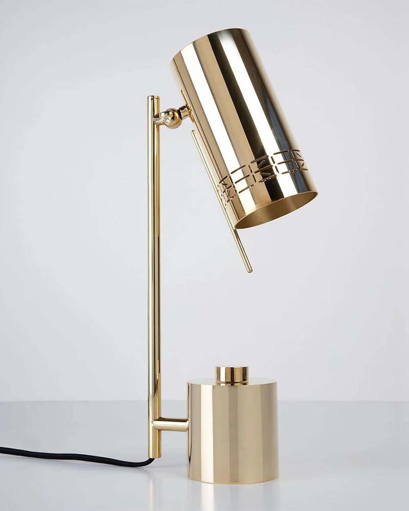 Sleek modern table lamp made of shiny gold metal, with a cylindrical shade on a vertical rod and a round weighted base, connected by a black power cord.