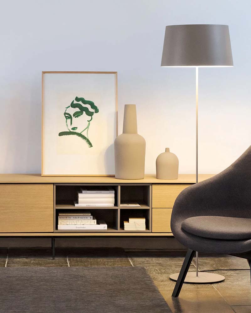 Modern living room vignette with a light wood media console, framed abstract artwork, decorative vases, floor lamp, and upholstered accent chair.