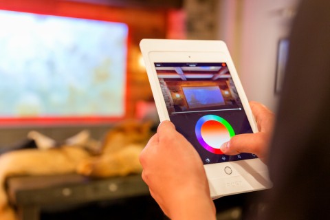 Person using a tablet to adjust smart lighting colors in a home theater. 