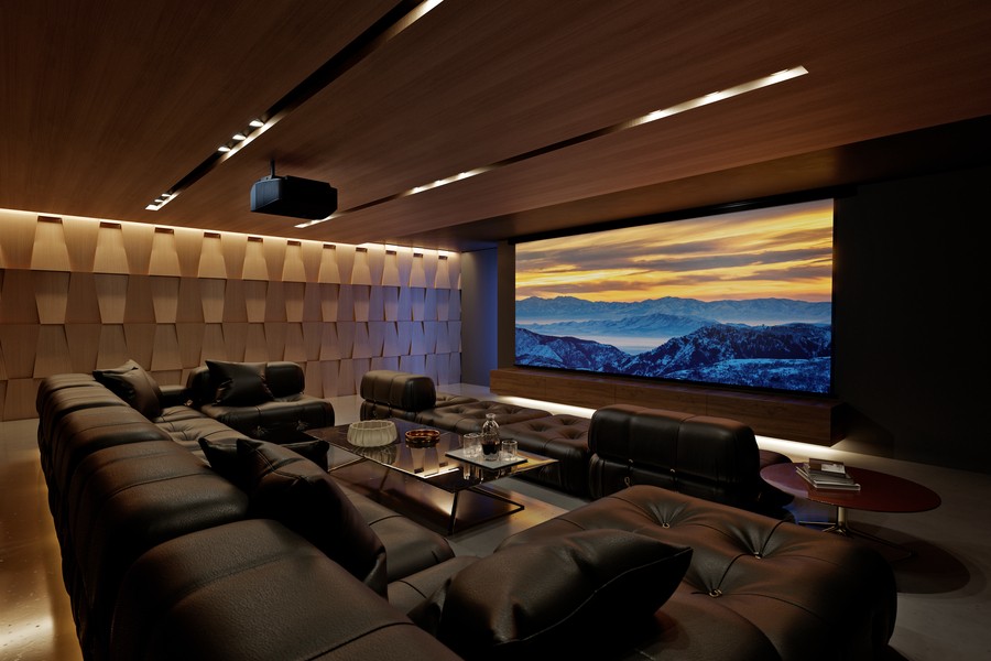 A home movie theater with a brown sectional, acoustic paneling, large movie screen, and Sony projector.