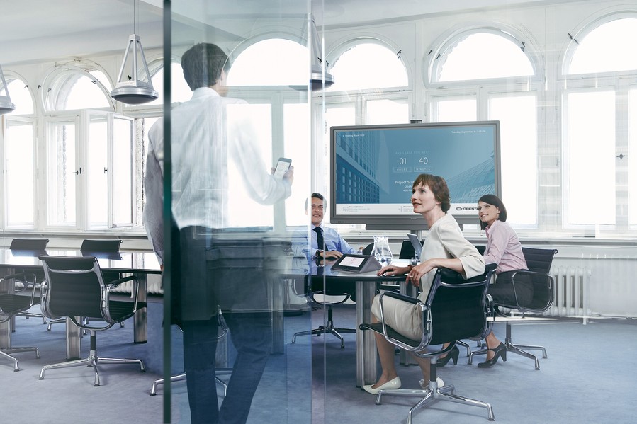 A group of people working in a boardroom featuring Crestron technology. 