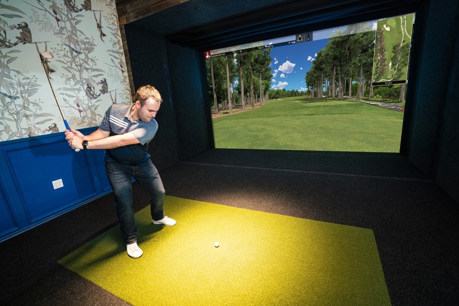 A man playing golf in a room using a golf simulator.
