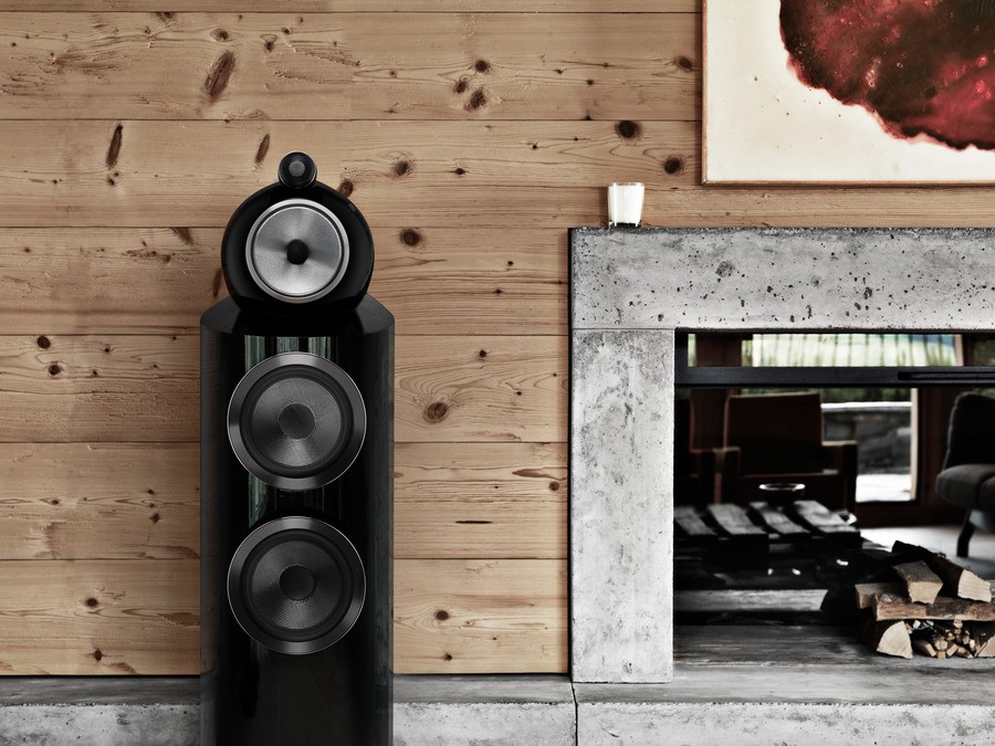 A gloss black 802 D3 Bowers and Wilkins speaker to the left of a fireplace.