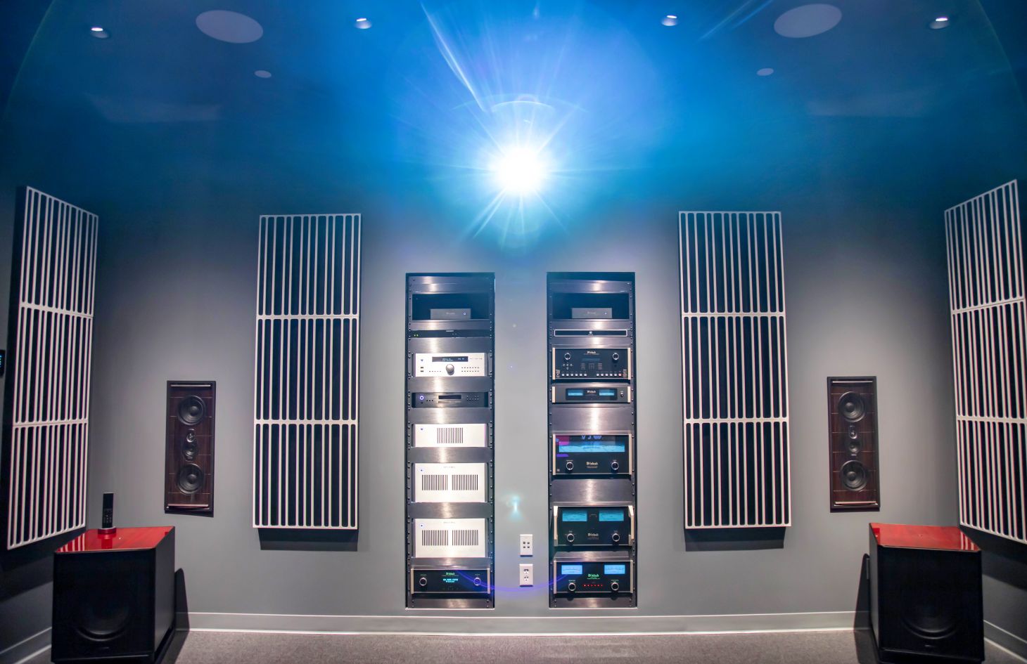 High-end home theater front wall featuring a ceiling-mounted projector, in-wall speakers, acoustic panels, and dual equipment racks with premium audio components.